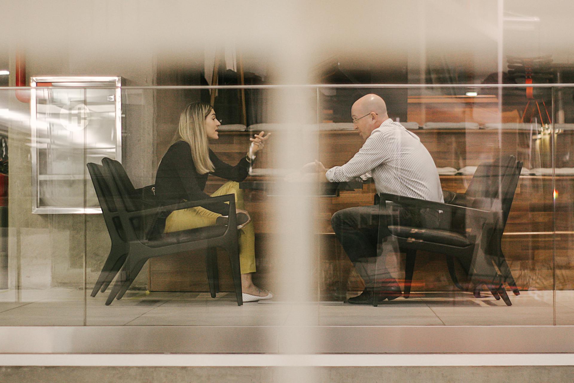 Two people engaged in an active professional discussion behind a glass office wall